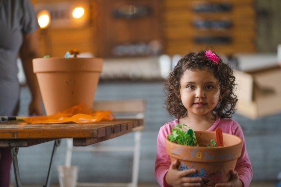 a young child holding a pot of herbs in a painted pot